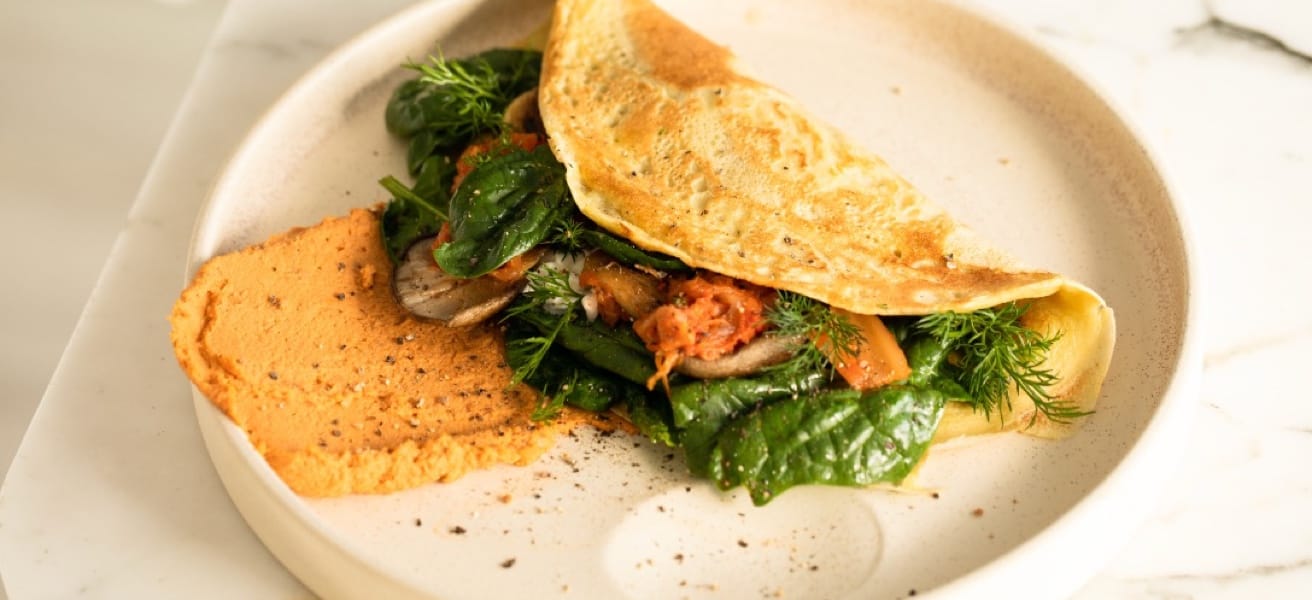 An omelette with leafy vegetables inside placed in a color white plate